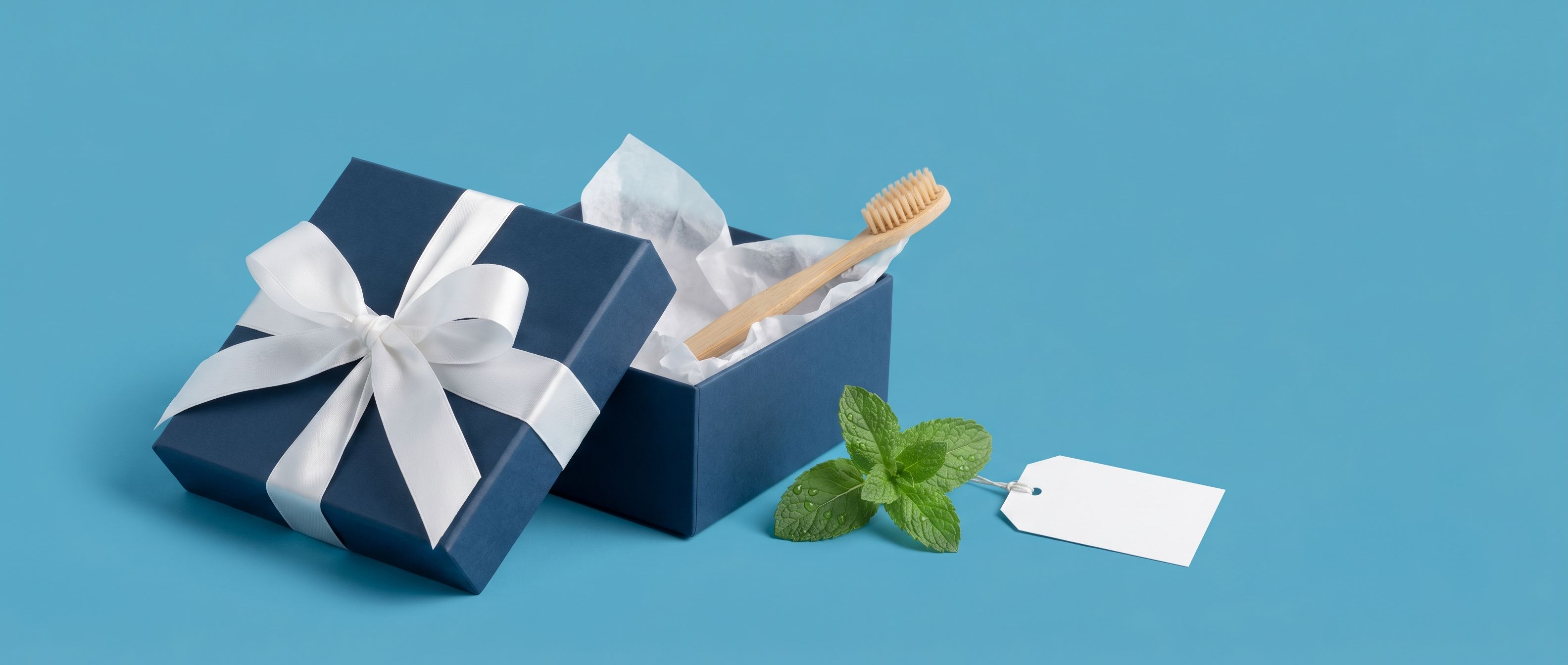 Navy gift box with white ribbon and a bamboo toothbrush peeking out, fresh peppermint beside, on a mid-blue background
