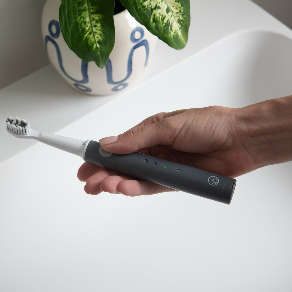 The Waken Sonic Toothbrush in Graphite Grey held in one hand, showing the mode lights